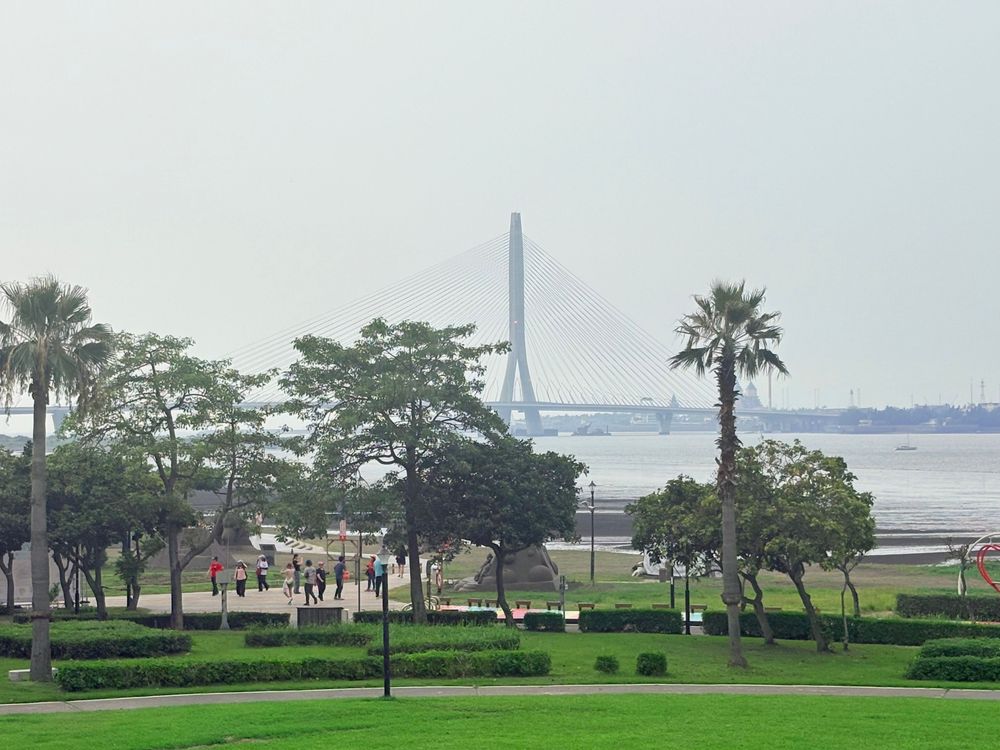 遠眺淡江大橋橫跨淡水河口，河岸綠意與城市景觀彼此交會。從八里的視角出發，看見自然、城市與人文共同交織的風景。（照片提供者：游子誼 / 拍攝日期：2026.08.11）
